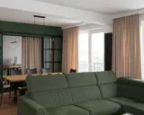 Jasne zasłony idealnie komponują się z zielonymi ścianami, tworząc przytulną atmosferę w salonie z jadalnią.